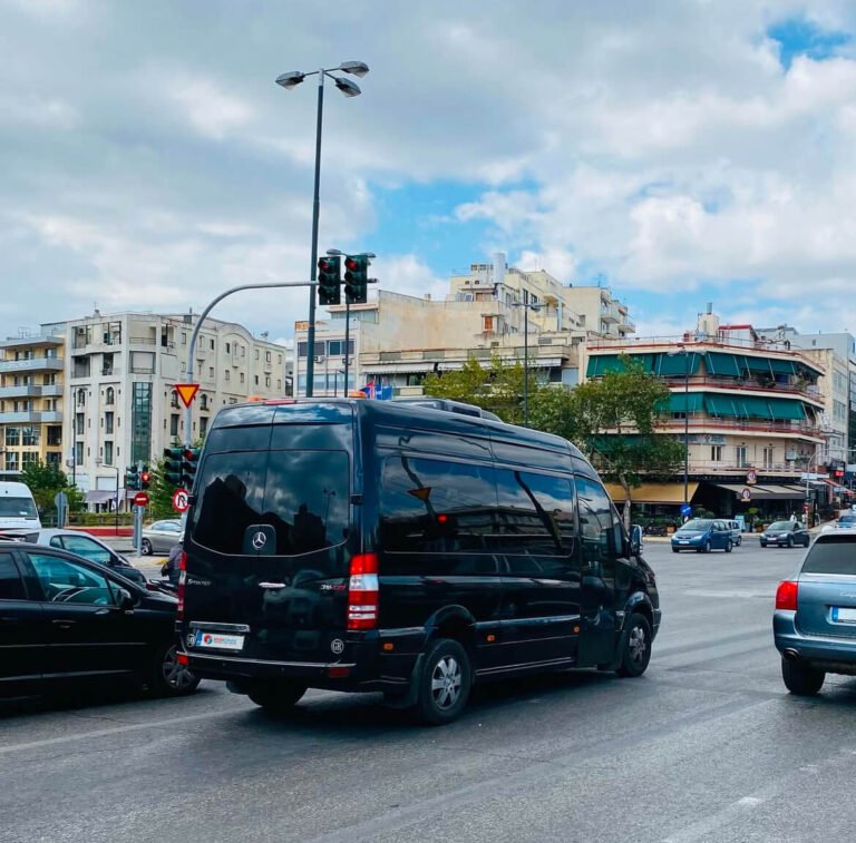 Black Sprinter minibus turns at busy city intersection with cars, buildings, and cloudy sky