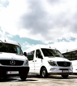 A fleet of white Mercedes-Benz minibuses parked in a lot under a partly cloudy sky